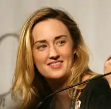 A blonde woman in her early thirties smiles at something off-camera.