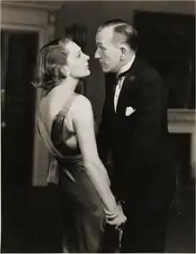 Youngish white couple in evening dress standing close together and looking into each other's eyes; greyscale.