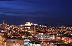 An illuminated cityscape alongside water seen at night from the air.