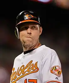 A man in a white baseball uniform with the word Orioles on it in cursive orange letters