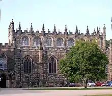 A two to three-storey high stone building. The building is topped with castellations and pinnacles