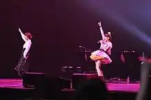 Two women performing on stage with a piano behind them