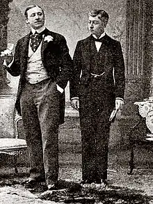 young white men, clean shaven, one in 1890s morning dress and the other in butler's outfit