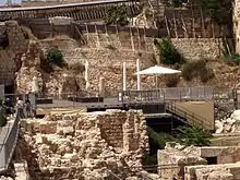 photograph depicting a platform raised over ruins and set against the backdrop of a high stone wall