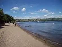 Sand and gravel beach in the foreground, with a sandspit in the background extending into a lake