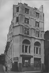 A narrow stone-faced façade with two bays of windows, arched at first floor level and decreasing in size on the floors above