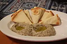 Baba ghanoush is a Levantine dish of cooked eggplant mixed with onions, tomatoes, olive oil and various seasonings, served here with pita bread.