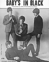 Black & white photo of the Beatles, with Lennon seated flanked by McCartney & Harrison and Starr reclining in front