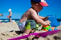 Image 19An infant boy playing with a toy dump truck at the beach. (from Boys' toys and games)