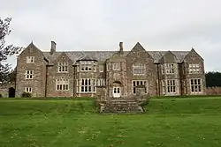 stone building with slate roof, with windows on central two bays, partly obscured by trees