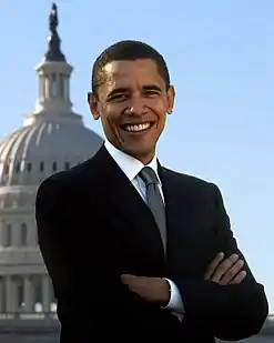 Photo of Obama smiling with his arms crossed, with the Capitol building and the sky in the background