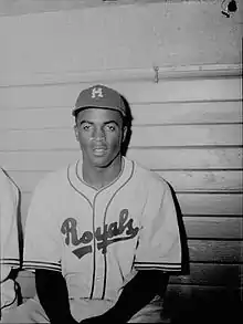 A black man in a baseball uniform with the words "Royals" and a baseball cap with the letter "M".