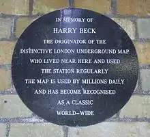 A circular plaque on a brick wall with the words: "In memory of Harry Beck the originate of the distinctive London Underground map who lived near here and used the station regularly. The map is used by millions daily and has become recognised as a classic world-wide."