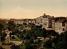 A park with trees and statuary, surrounded by multi-story buildings