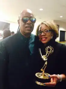 Bernadette Bascom holding Emmy and accompanied by Stevie Wonder