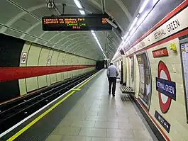 The interior of a building with a rounded roof and walls, a railway track on the left, some doors on the right, and a man walking in the middle