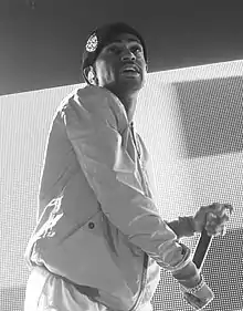  A grey photo of a man on a stage holding a microphone in his left hand.