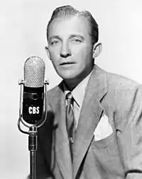 A vintage photo of Bing Crosby wearing a suit and singing into a CBS microphone.