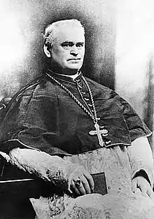 Bishop Manogue seated with a breviary in traditional choir dress, cassock and rochet.