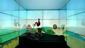 A man sleeps in a black bed, surrounded by three screens depicting a cartoon countryside sunrise with a rooster about to crow.