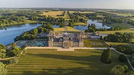 Exterior of a large English Baroque palace fronted by lawns