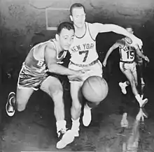 Two basketball players go after a basketball, while another player is watching from behind