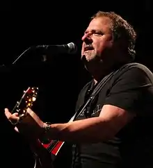 Songwriter Bob DiPiero, holding a guitar and singing into a microphone