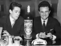 Belgian singers Jacques Brel and Bobbejaan Schoepen wear modified pompadour hairstyles, suits with sharply peaked lapels, and patterned ties, 1955.