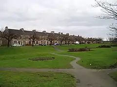 A row of terraced housing behind a green lawn and a row of trees.