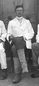 Black-and-white photograph of a man in a white shirt and dark trousers, seated, facing the camera