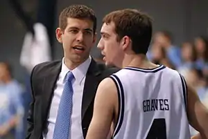 Stevens looks at a player as he talks with him. The players' eyes are turned toward the basketball game to Stevens's left.