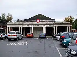 A red-bricked building with "BRENT CROSS STATION" written on it and light grey pillars making up the facade all under a blue sky with white clouds