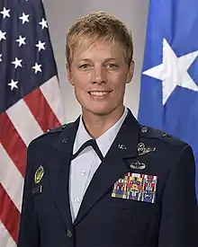 A portrait photograph of a white woman in a blue US Air Force uniform; she is smiling while facing and looking into the camera.