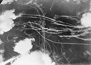 A picture of a piece of sky with several clouds and many condensation trails caused by many aircraft. Each trail curves around the other indicated an air battleItalic text