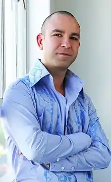 Portrait of Schiavi in a light-blue open collar shirt with his arms crossed across his chest.