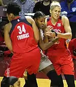 Thomas and Delle Donne wearing bright red uniforms attempt to squeeze Brunson out as she emerges between them