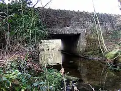 ancient stone bridge with square arch supported by a beam, over a small calm stream