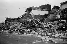 A destroyed brick building, with debris piled high along the side of the adjacent road