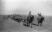 A column of around a dozen Foreign Legion troops on foot, followed by a similar number mounted on donkeys and led by two mounted officers/NCOs proceeding along a road