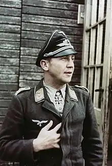 Color portrait of a man wearing a peaked cap, military uniform with an Iron Cross displayed at his neck.