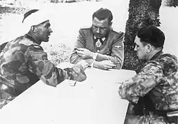 Three men sitting at a table, one apparently with his head bandaged