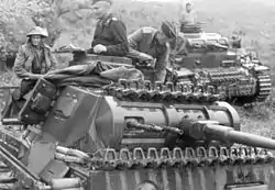 Black and white photo of two tanks with people standing in their cupolas or sitting on them