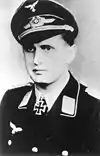 A man wearing a peaked cap and military uniform with an Iron Cross displayed at the front of his uniform collar.