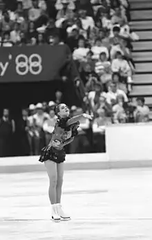 A female figure skater points with her right arm as she performs