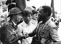 A youth representative of the PRG greets a young man from a Soviet-aligned unidentified African nation. Both are attending a 1973 World Youth Conference held in East Germany and organised by the Free German Youth.