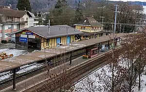 Yellow two-story building with hip roof next to double-track railway line and island platform