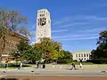 Burton Tower against a blue sky with trees just beginning to turn autumn colors. Students are walking in the foreground