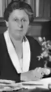 A posed black-and-white photograph of a woman seated at a desk