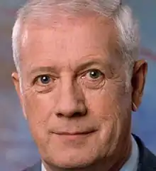 Late middle-aged man with grey hair wearing a white dress shirt and a grey suit jacket