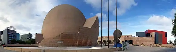 The OMNIMAX dome (a great sand-colored sphere) with tall buildings in the background and the paved plaza in the foreground